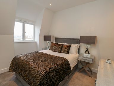 A bedroom with a bed with patterned bedspread and pillows and two bedside tables with lamps at Harbourside Haven Penthouse 1 in Weymouth