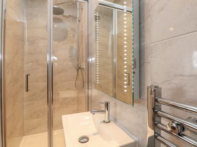 A bathroom with a shower enclosure sink with faucet mirror with lights and a chrome towel rack at Harbourside Haven Penthouse 1 in Weymouth