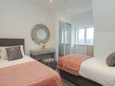 A bedroom with two beds pink blankets a dressing table with a round mirror and a window at Harbourside Haven Penthouse 1 in Weymouth