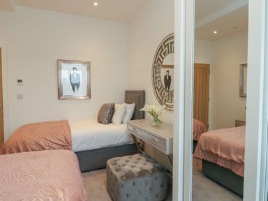 A bedroom with two beds a desk mirror and a cushioned stool at Harbourside Haven Penthouse 1 in Weymouth