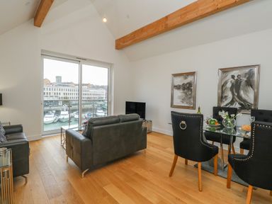 A living room with black leather sofas and a glass dining table with black chairs at Harbourside Haven Penthouse 2 in Weymouth