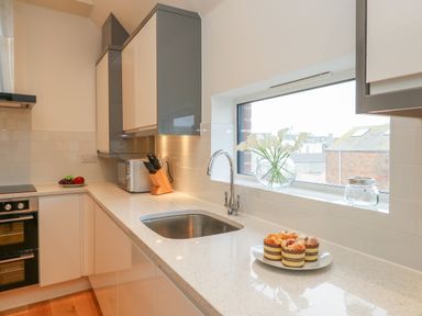 A kitchen countertop with a sink a plate of muffins a knife block and a microwave by a window with flowers at Harbourside Haven Penthouse 2 in Weymouth