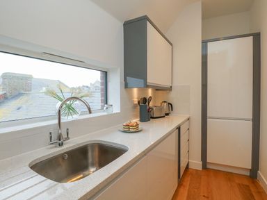 A kitchen with a sink under a window with flowers and a counter with kitchen appliances at Harbourside Haven Penthouse 2 in Weymouth