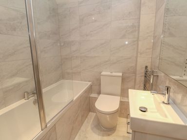 A bathroom with a bathtub shower combination a toilet and a sink at Harbourside Haven Penthouse 2 Weymouth