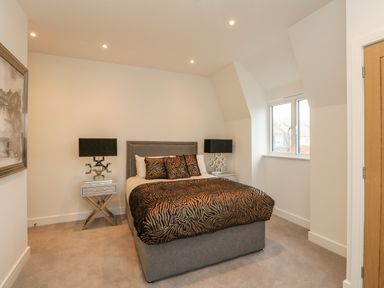 A bedroom with a bed with animal print bedding two bedside tables with lamps and a window at Harbourside Haven Penthouse 2 in Weymouth