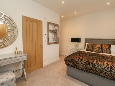 A bedroom with a bed with animal print bedding a bedside table with a lamp a wooden door a mirrored dressing table with decorative items and a wall mirror at Harbourside Haven Penthouse 2 Weymouth