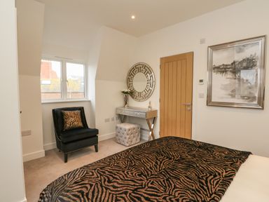 A bedroom with a bed covered in a patterned blanket a black chair with a matching cushion a small table with a round mirror and a tufted stool at Harbourside Haven Penthouse 2 in Weymouth