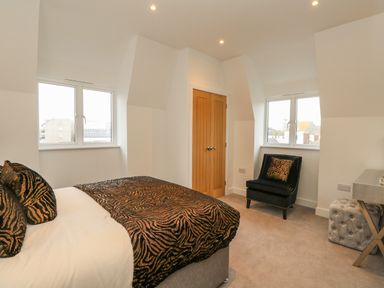 A bedroom with a bed, armchair, closet doors, two windows, and a desk at Harbourside Haven Penthouse 2 in Weymouth
