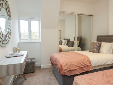 A bedroom with two beds a mirrored wardrobe a window a desk with decorations and a circular wall mirror at Harbourside Haven Penthouse 2 in Weymouth