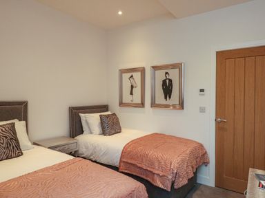 A bedroom with two single beds with pink bedspreads two framed pictures on the wall and a wooden door at Harbourside Haven Penthouse 2 in Weymouth