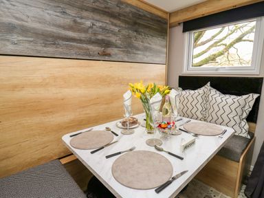 A dining table set with plates cutlery and glasses next to a window with patterned cushions at Woodland Escape in Rhayader