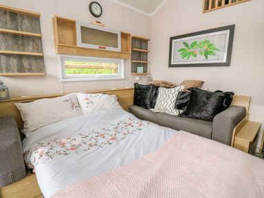A bed with floral bedding and a sofa with cushions in a small room at Woodland Escape in Rhayader