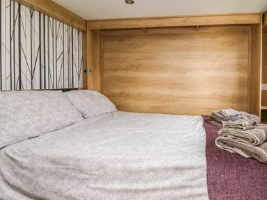A bedroom with a bed covered in white bedding and towels on a purple blanket at Woodland Escape in Rhayader