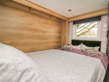 A bedroom with a bed covered with a blanket and pillows next to a window showing tree branches at Woodland Escape in Rhayader