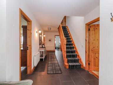 A hallway with stairs covered with a runner and a console table along the wall at Cherry Blossom Cottage in Quilty County Clare