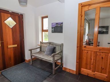 An entryway with a wooden bench and cushion near a wooden door and glass-paneled wooden door at Cherry Blossom Cottage Quilty County Clare
