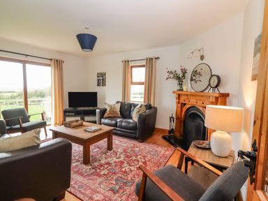 A living room with leather sofas wooden coffee table patterned rug fireplace and television at Cherry Blossom Cottage in Quilty County Clare