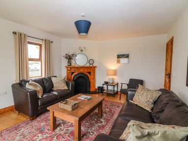 A living room with leather sofas a wooden coffee table a fireplace and a window with curtains at Cherry Blossom Cottage in Quilty County Clare