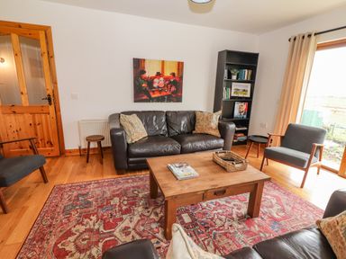 A living room with leather sofa wooden coffee table red patterned rug and bookshelf at Cherry Blossom Cottage in Quilty County Clare