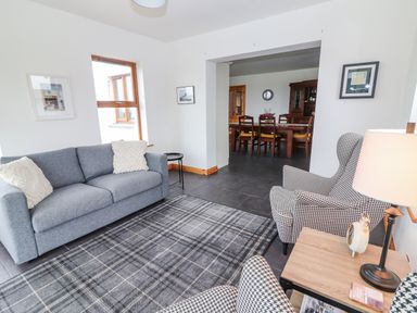 A sitting room with a gray sofa, patterned armchairs, a checkered rug, and a side table with a lamp and clock at Cherry Blossom Cottage in Quilty County Clare