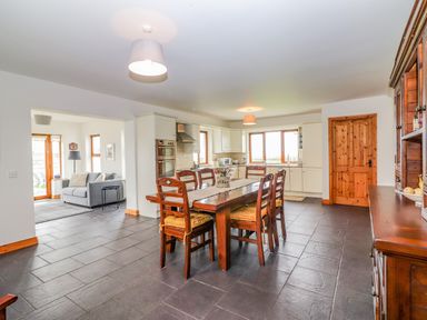 A kitchen dining area with a wooden table and six chairs cushions on chairs and a gray tiled floor at Cherry Blossom Cottage in Quilty County Clare