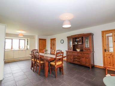A dining room with a wooden table and chairs a wooden cabinet and kitchen area with a window at Cherry Blossom Cottage in Quilty County Clare