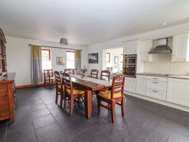 A kitchen with white cabinets a wooden dining table with chairs and yellow cushions at Cherry Blossom Cottage in Quilty County Clare
