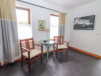 A corner with two wooden chairs and a round table between them with a lamp a painting and a photo on the wall at Cherry Blossom Cottage in Quilty County Clare
