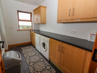 A utility room with wooden cabinets washing machine dryer and a waste bin at Cherry Blossom Cottage in Quilty County Clare