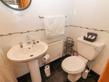 A bathroom with a pedestal sink a towel rail with a white towel a toilet with toiletries on top and a toilet paper holder at Cherry Blossom Cottage in Quilty County Clare