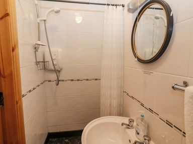 A small bathroom with a shower, sink, round mirror, and a towel rack at Cherry Blossom Cottage in Quilty, County Clare