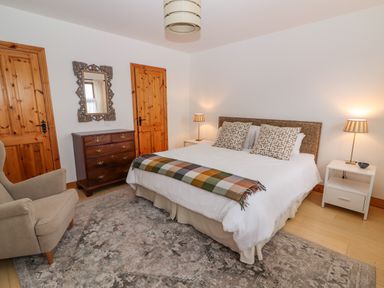 A bedroom with a bed, armchair, chest of drawers, mirror, two bedside tables with lamps at Cherry Blossom Cottage in Quilty County Clare