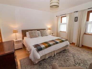 A bedroom with a bed two bedside tables with lamps two windows with curtains and a wooden chest of drawers at Cherry Blossom Cottage in Quilty County Clare