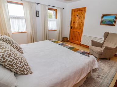 A bedroom with a bed pillows armchair wooden door and two windows at Cherry Blossom Cottage in Quilty County Clare
