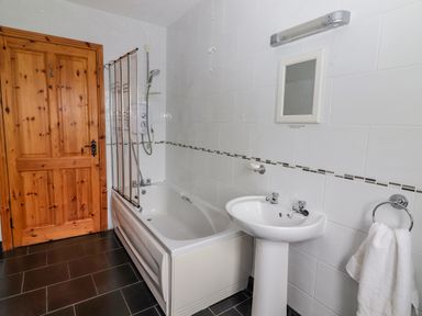 A bathroom with a bathtub shower combination sink mirror and wooden door at Cherry Blossom Cottage in Quilty County Clare