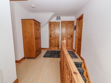 A hallway with wooden doors a wooden wardrobe and stairs with a wooden banister at Cherry Blossom Cottage in Quilty County Clare
