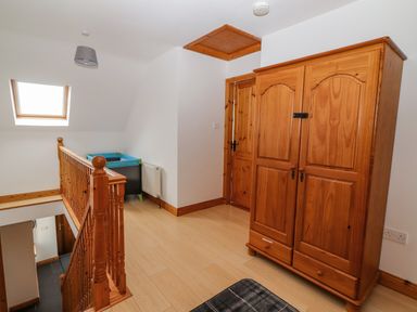 A small landing area with a wooden wardrobe and a wooden banister next to a skylight window at Cherry Blossom Cottage in Quilty County Clare