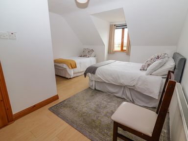 A bedroom with two single beds a window chair and a rug at Cherry Blossom Cottage in Quilty County Clare