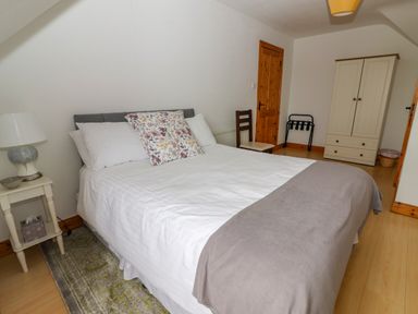 A bedroom with a double bed a bedside table with a lamp a chair a wardrobe and a wooden door at Cherry Blossom Cottage in Quilty County Clare