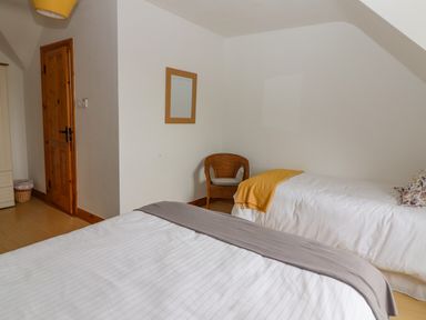 A bedroom with two beds a wicker chair a wooden door and a mirror on the wall at Cherry Blossom Cottage in Quilty County Clare