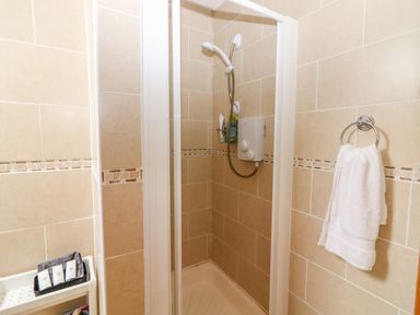 A tiled bathroom shower area with a white towel hanging on a ring and toiletries on a shelf at Cherry Blossom Cottage in Quilty County Clare
