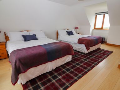 A bedroom with two double beds wooden nightstands table lamps a window and a red plaid rug at Cherry Blossom Cottage in Quilty County Clare