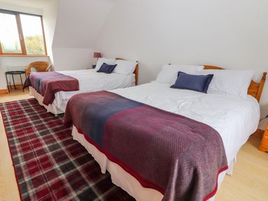 A bedroom with two double beds a chair and a window at Cherry Blossom Cottage in Quilty County Clare