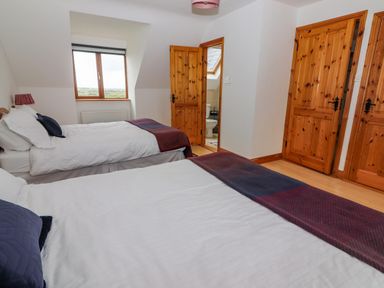 A bedroom with two beds wooden doors and a window at Cherry Blossom Cottage in Quilty County Clare