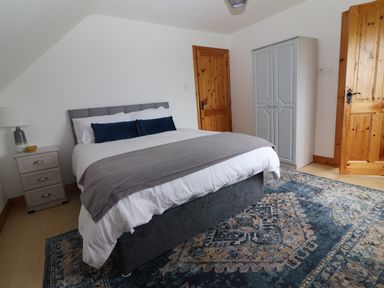 A bedroom with a double bed side table with a lamp and a wardrobe at Cherry Blossom Cottage in Quilty County Clare