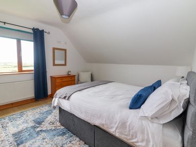A bedroom with a bed pillows a wooden dresser a mirror curtain and a rug at Cherry Blossom Cottage in Quilty County Clare