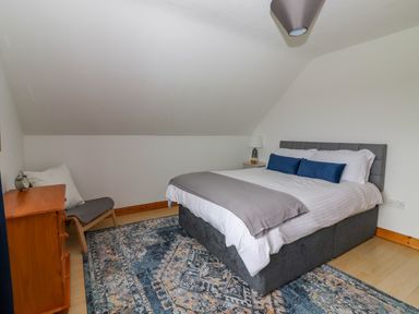A bedroom with a bed a dresser a chair and a rug at Cherry Blossom Cottage in Quilty County Clare