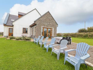 An outdoor seating area with blue plastic chairs and a dining table next to a house with stone and white walls at Cherry Blossom Cottage in Quilty County Clare
