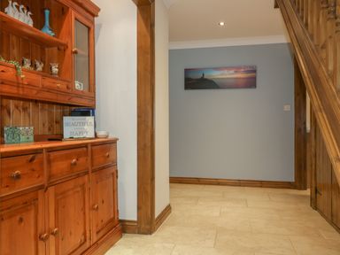 A hallway with wooden cabinetry on the left a photo on the wall and a wooden staircase on the right at Meadowside in Goonhavern