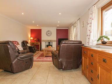 A living room with brown leather armchairs a wooden coffee table a red patterned rug and a wooden cabinet by a window at Meadowside in Goonhavern